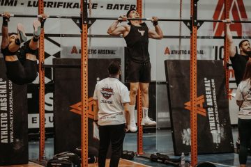 Athletes performing pull-ups in a CrossFit competition, judged by officials, showcasing strength and endurance.